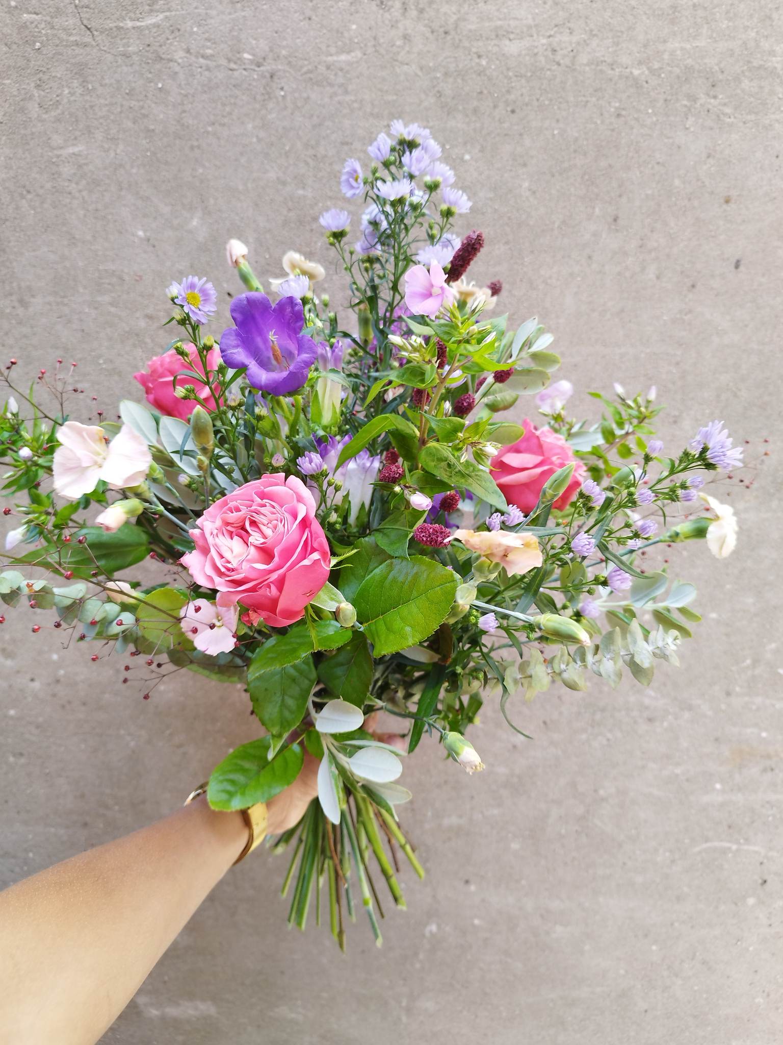 Luftig og livlig buket bundet med årstidens friske lilla, rosa og grønne blomster. 