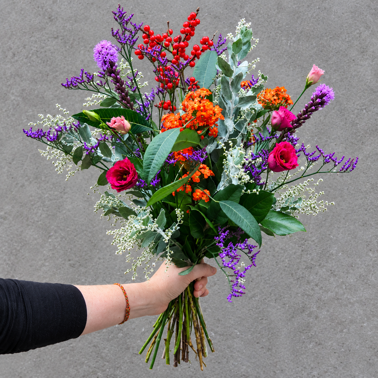 Buket bundet med blomster i lilla, blå, røde og orange farver. 