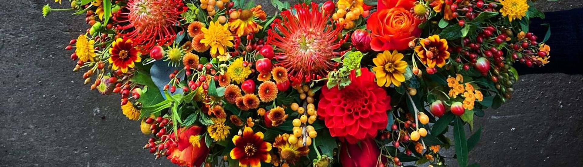 Begravelseskrans bundet med efterårsblomster i varme og stærke farver.