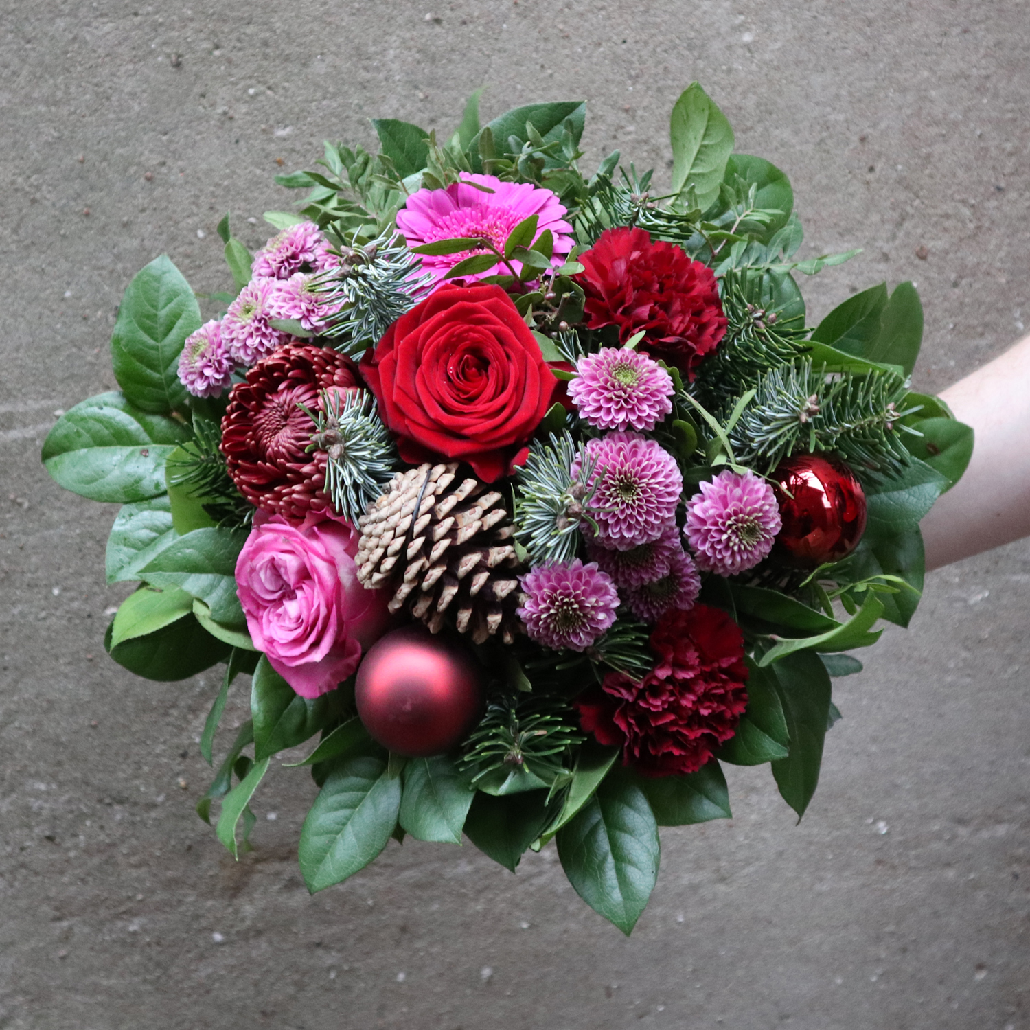 Julebuket med blomster rødilla farver med vintergrønt og kogler. 