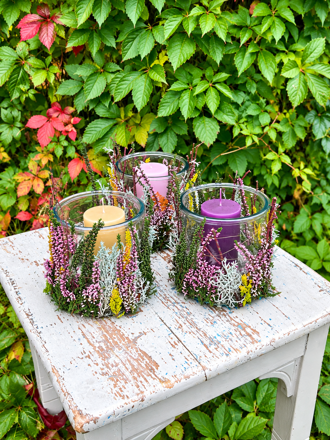 Lyngglas med bloklys dekoreret med naturlig lyng og botaniske materialer på rustikt havebord.