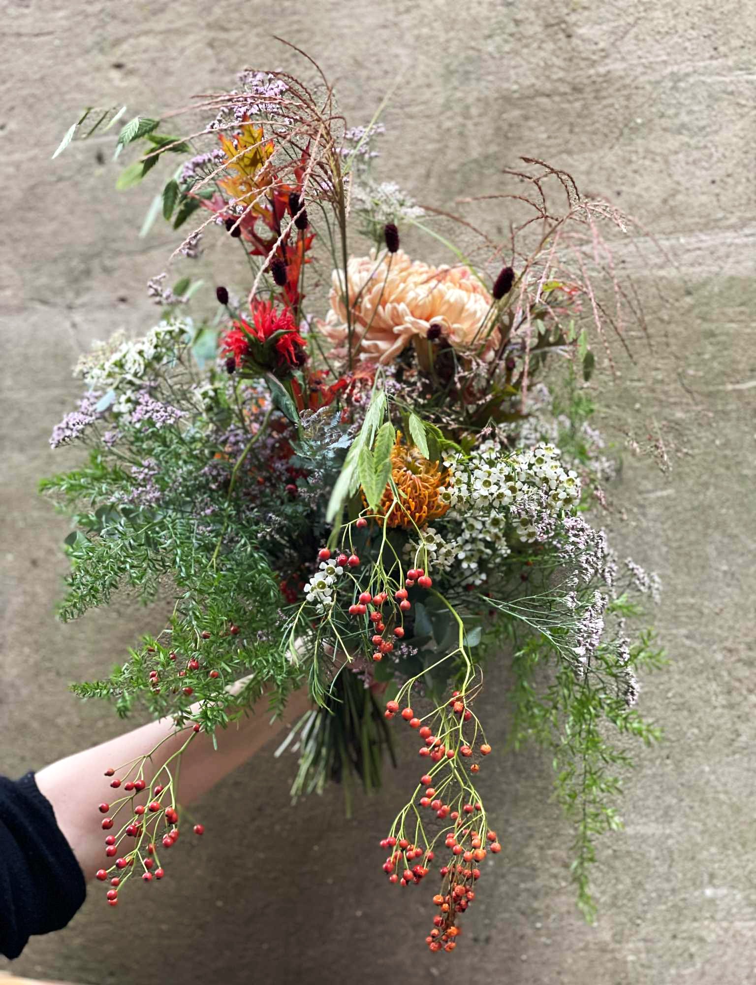Buket bundet med blomster i lilla, blå, røde og orange farver. 