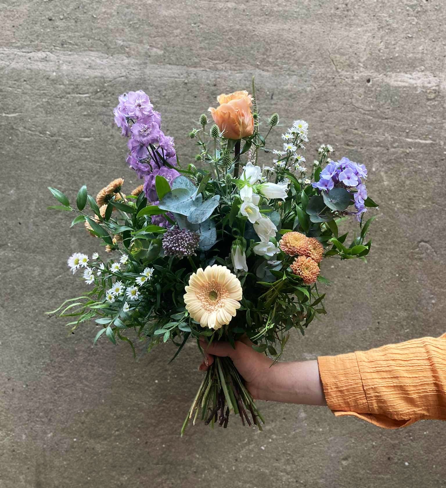 Vild kondolencebuket bundet med blomster i pastelfarver. 