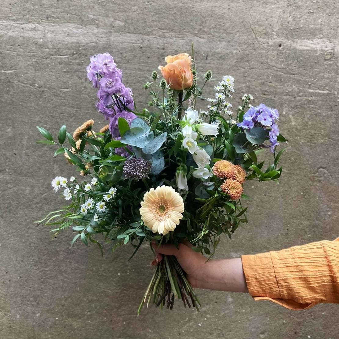 Vild kondolencebuket bundet med blomster i pastelfarver.