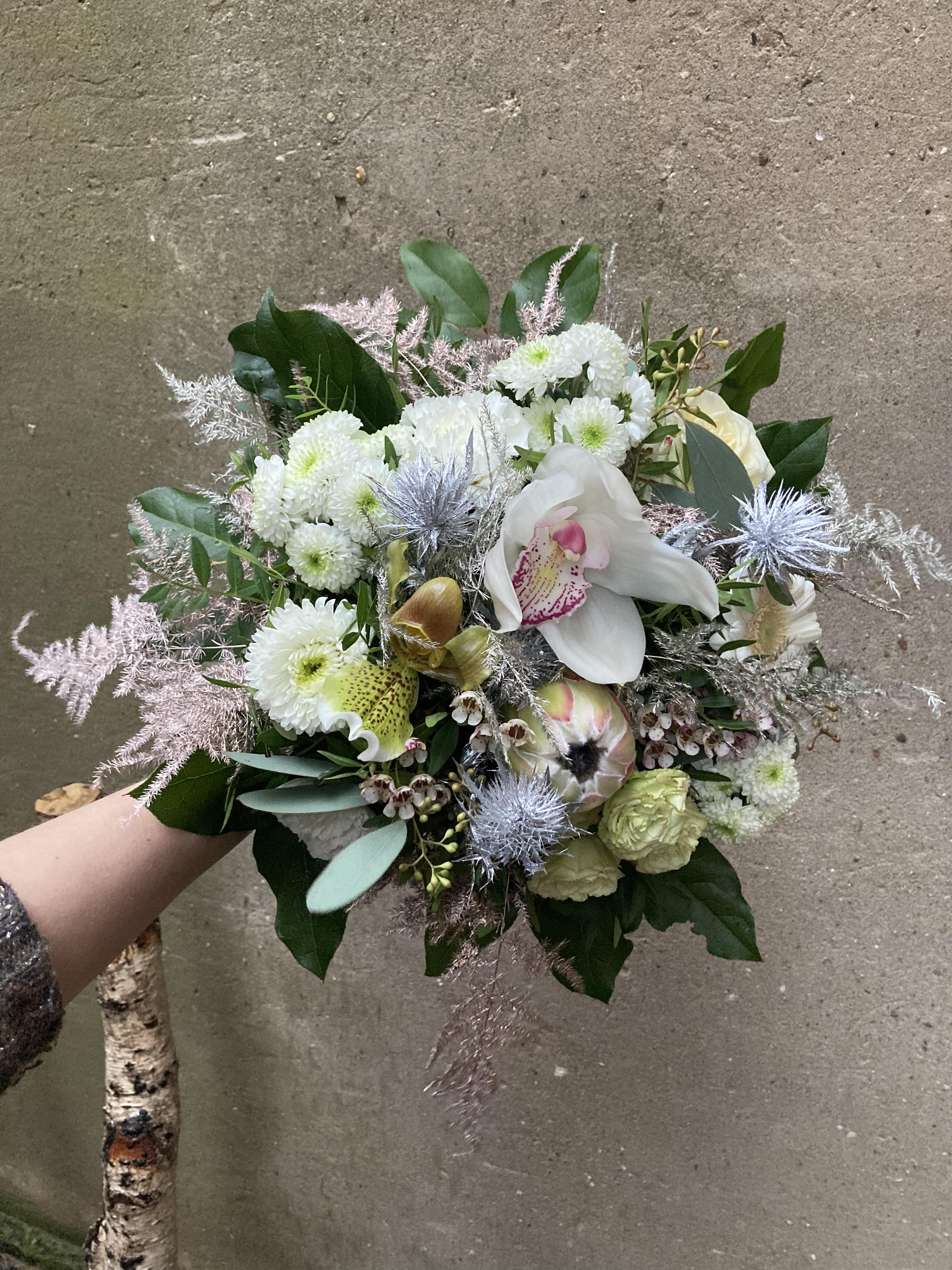 Tæt og sprudlende nytårsbuket bundet med hvide blomster og sølvfarver. 