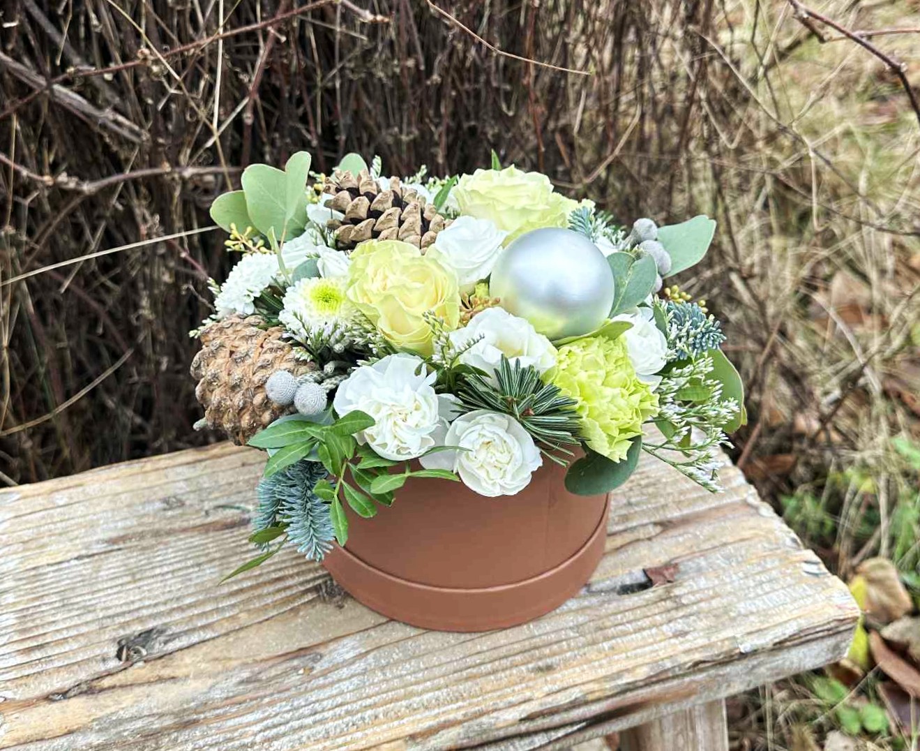 Hvid julehatteæske med julekugler, kogler og blomster i lyse farver. 