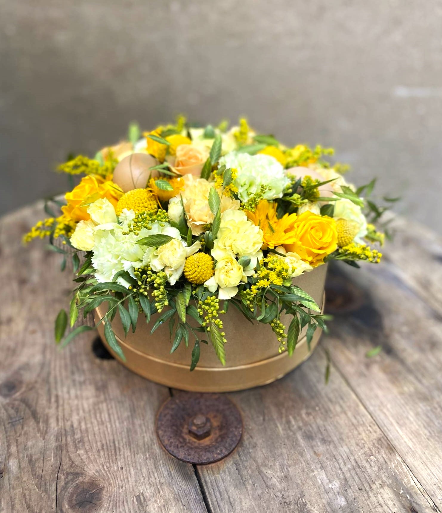 Stor hatteæske med gule og lyse nuancer fra Årstidens Blomster i Helsinge. Den står på en kabeltromle af træ.