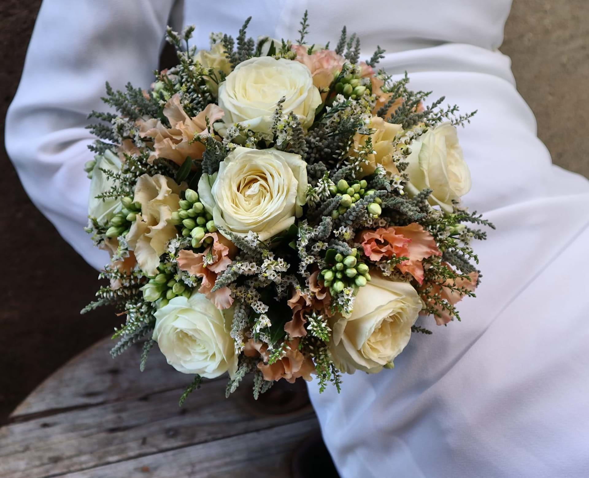 Hvid brud holder en romantisk og lys brudebuket med let fald, og roser i forskellige cremede nuancer.