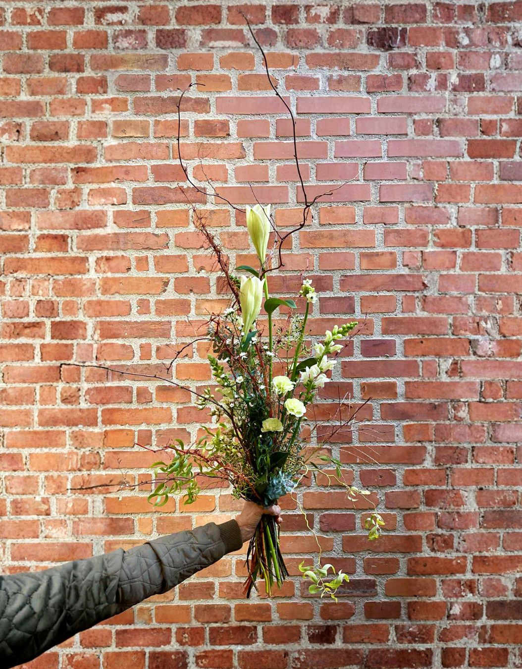 Buket bundet med lyse blomster og grene. Buketten har et højt og livligt udtryk. 