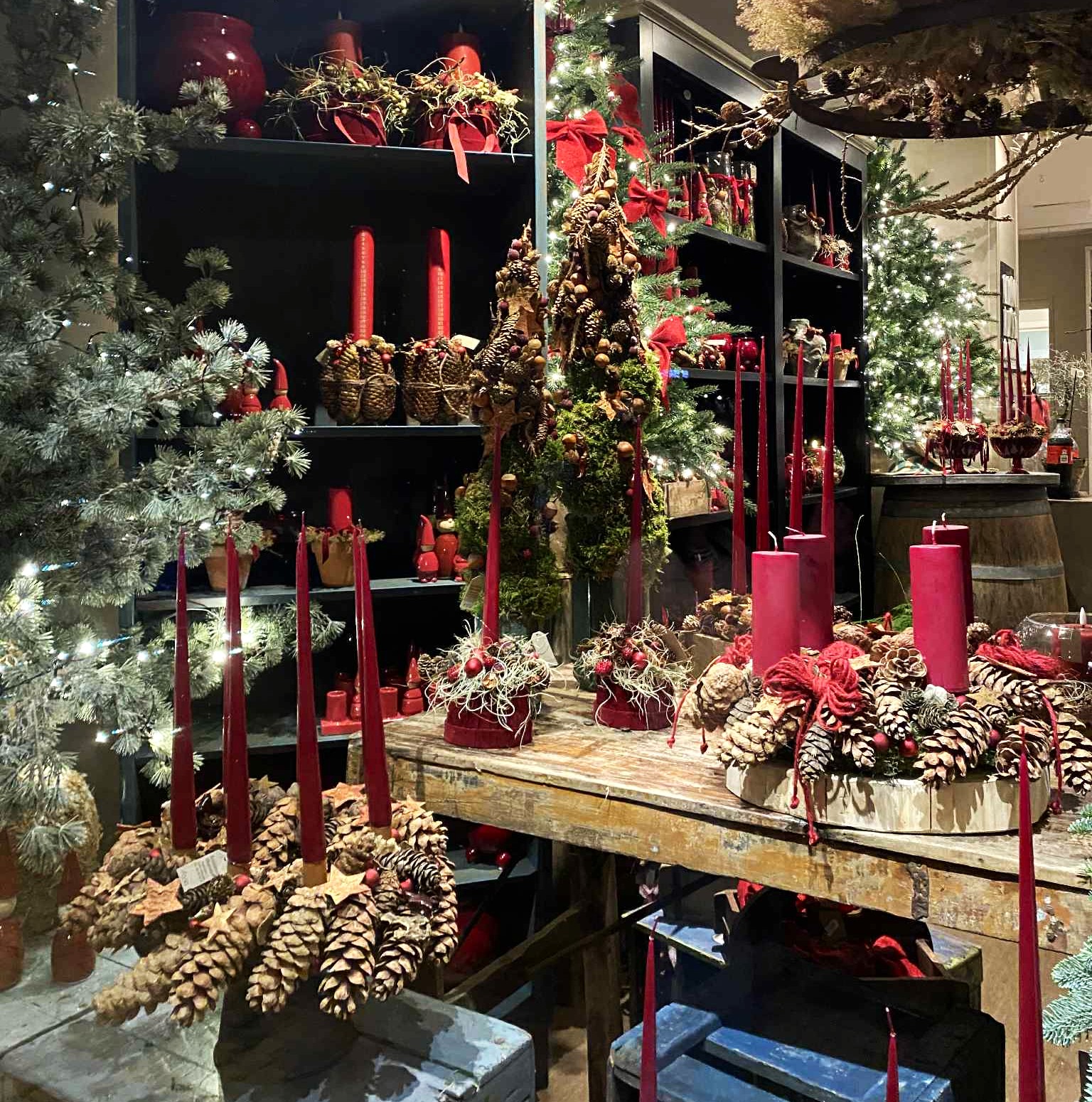 Borde og reoler fyldt med røde adventskranse, juledekorationer, grantræer og pynt. 