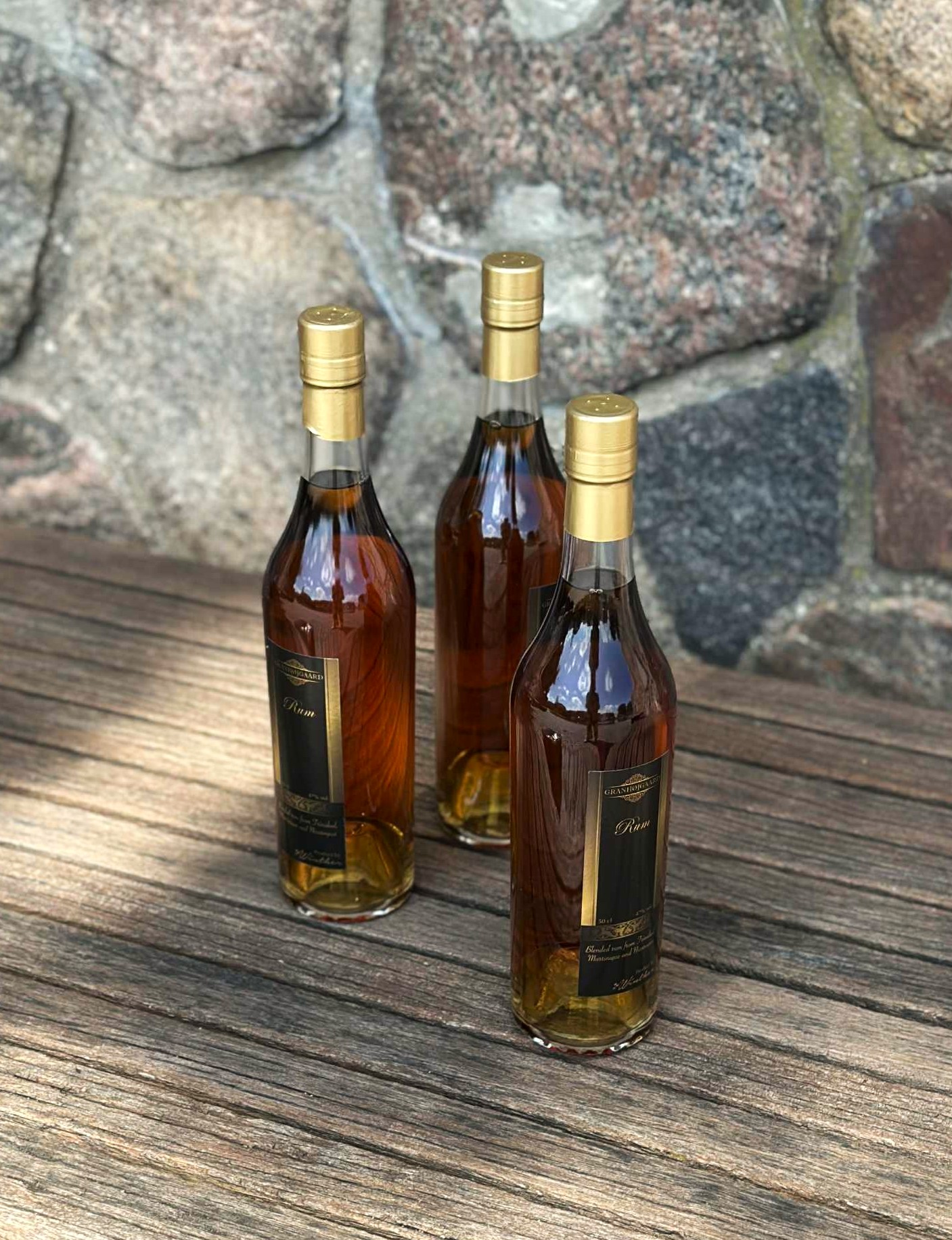 Tre flakser mørk Granhøjgaard rom står samlet på en rustik træbænk.  