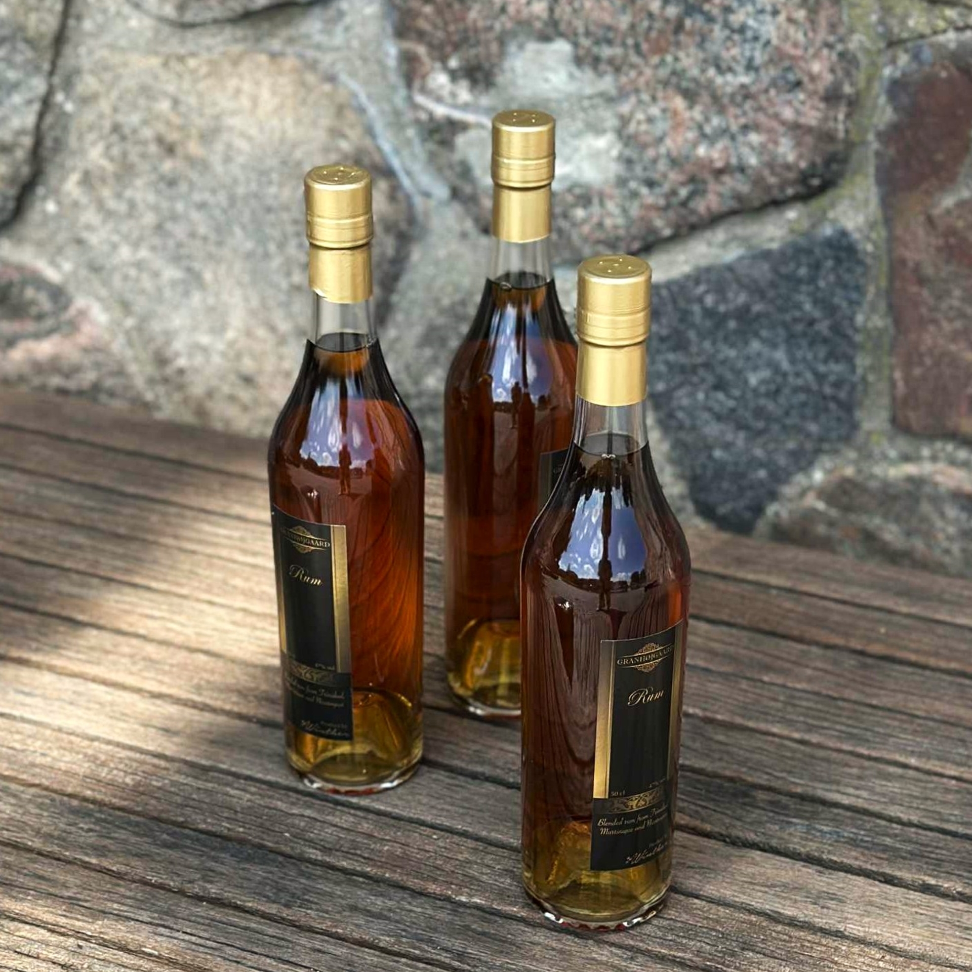 Tre flakser mørk Granhøjgaard rom står samlet på en rustik træbænk.