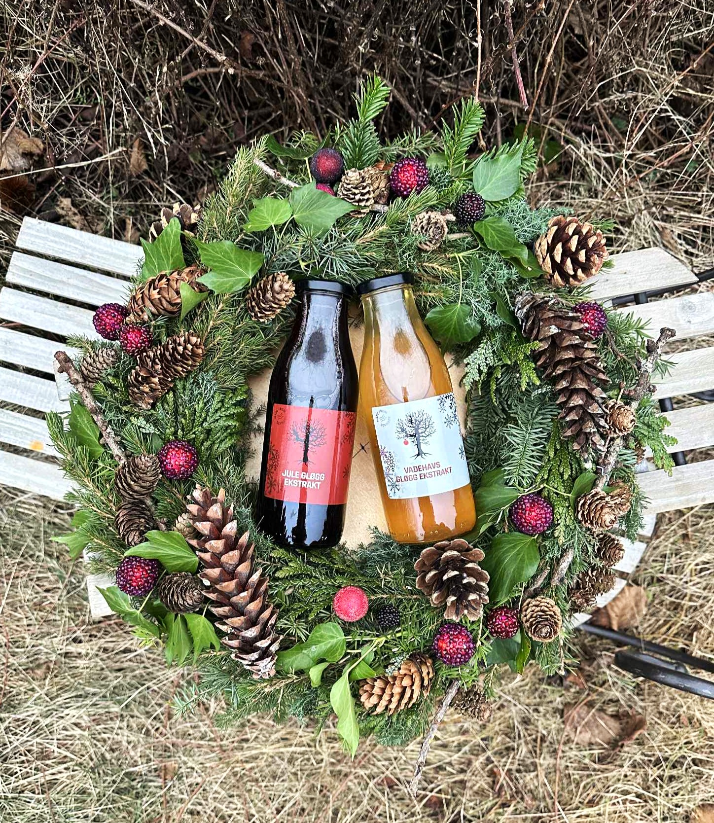 Hr. Skov Jule Gløgg Ekstrakt og Hr. Skov Vadehavs Gløgg Ekstrakt er omkranset af en julekrans med kogler, gran og julepynt. 