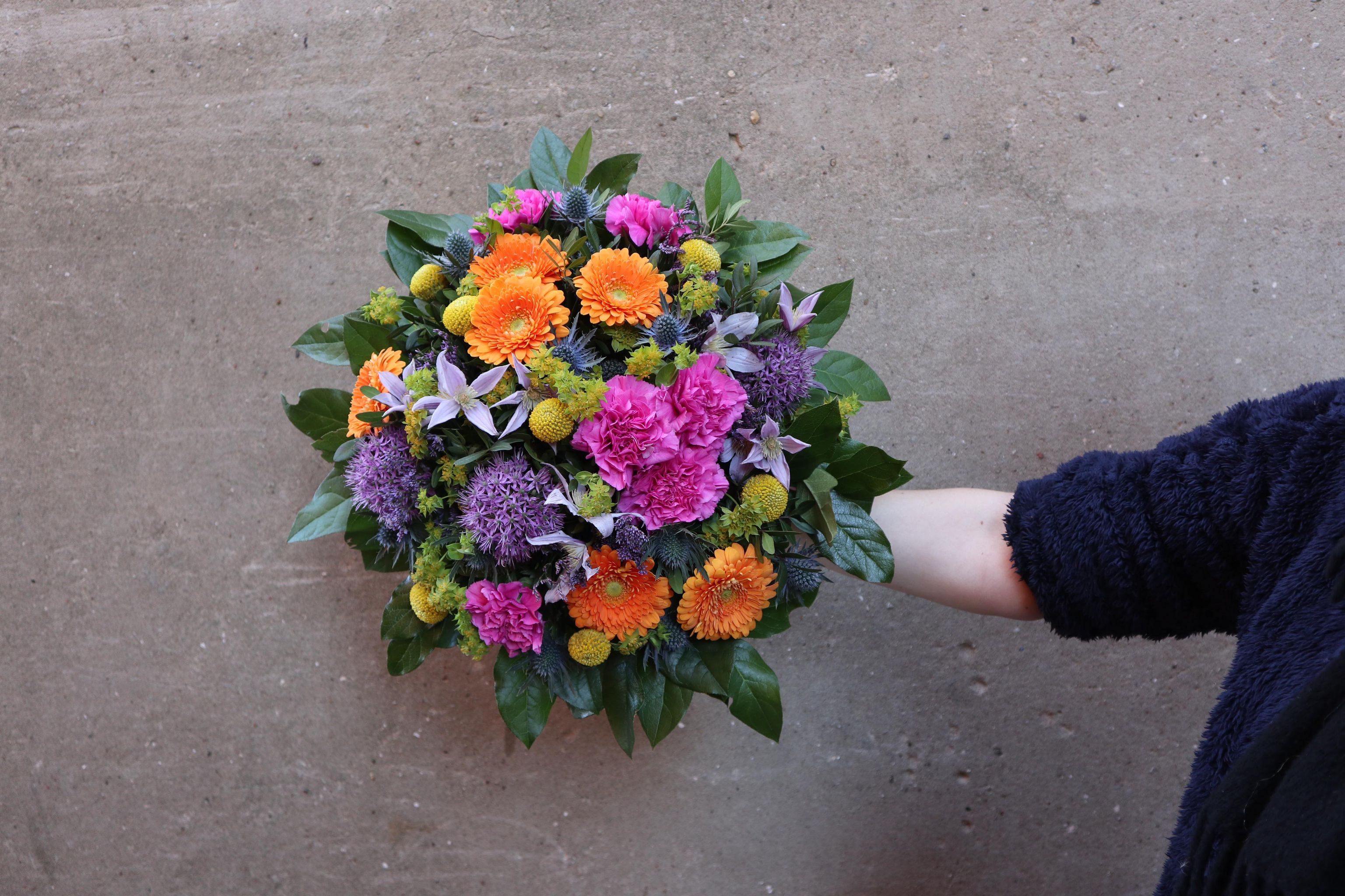 Rund & farverig buket med orange, lilla og lyserøde blomster. 