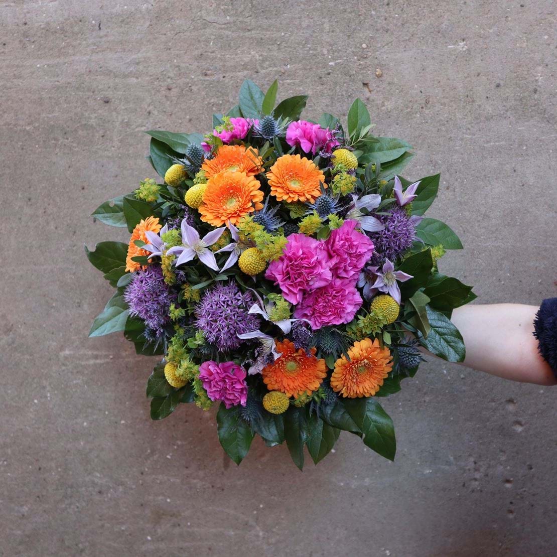 Rund & farverig buket med orange, lilla og lyserøde blomster.
