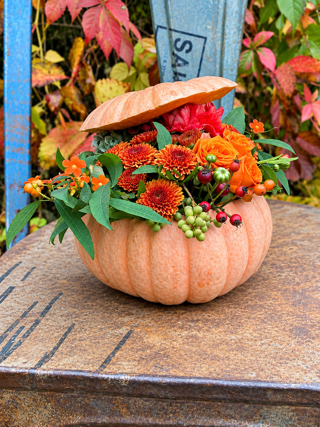 Lyst orange halloween græskar er pyntet og fyldt med efterårsblomster i varme nuancer. 