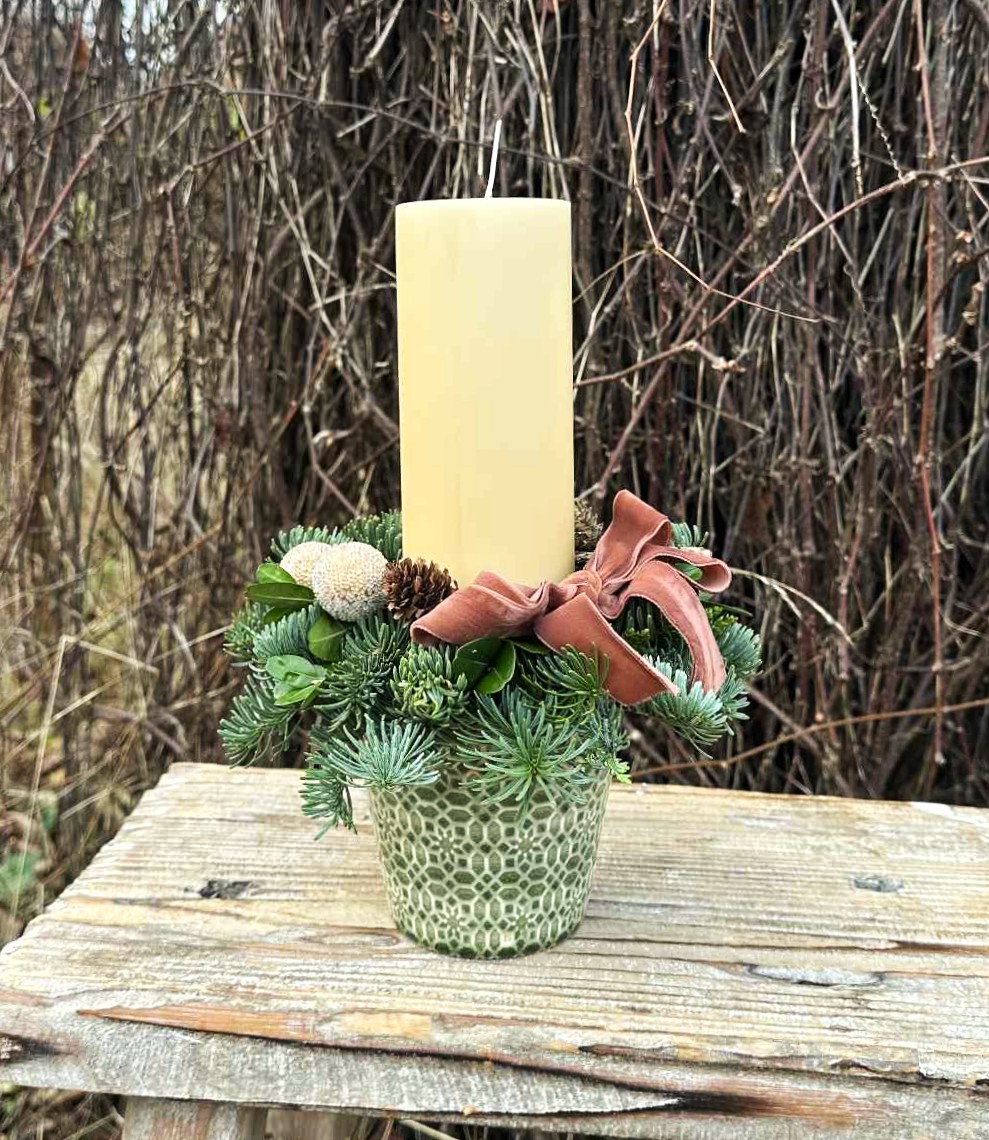 Juledekoration i grøn potte med gran, kogler og et cremefarvet lys. 