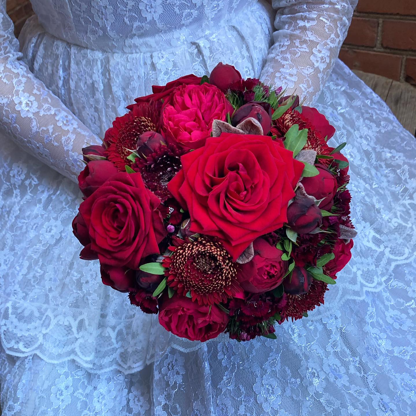 Tætbundet og rund brudebuket med blomster i dybe røde nuancer. 